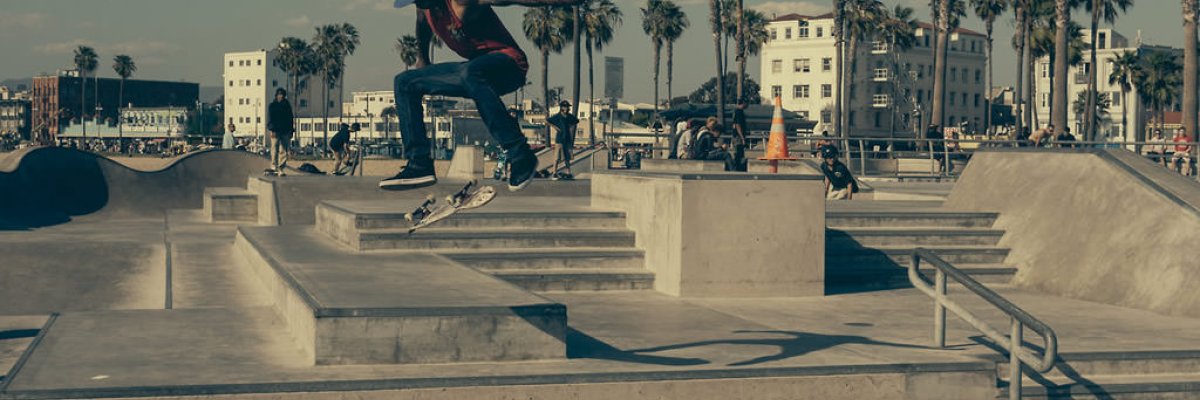 A skateboarder in mid-air at a busy outdoor skatepark lined with palm trees